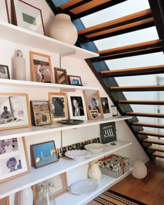 Floating shelves under stairway filled with framed photos and eclectic decor