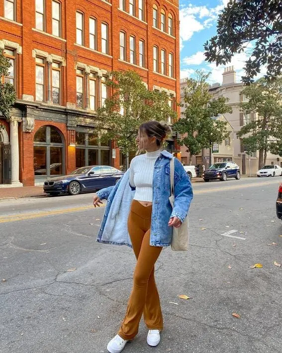 A woman in a cozy autumn outfit with a flared jacket and denim pants. 