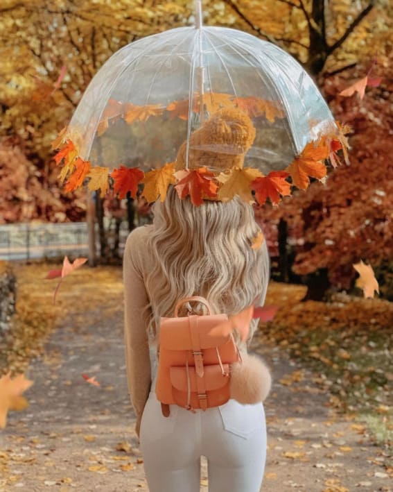 Woman in a chic fall outfit with a transparent umbrella and cozy backpack. 