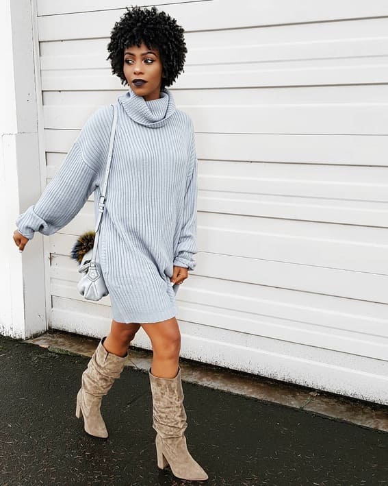 A woman is wearing an over-sized grey turtleneck sweater with the most comfortable boots. 