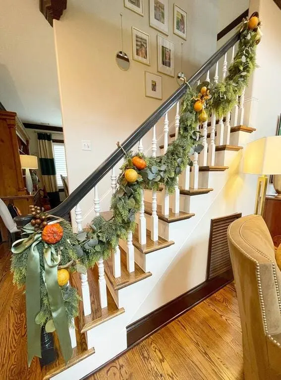 A beautifully decorated staircase featuring a lush garland of greenery accented with citrus fruits and eucalyptus, adding a fresh and festive fall touch. 