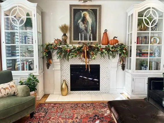 A beautifully decorated fall mantel with pumpkins, a lush garland, and a vintage painting above, creating a cozy, seasonal atmosphere. 