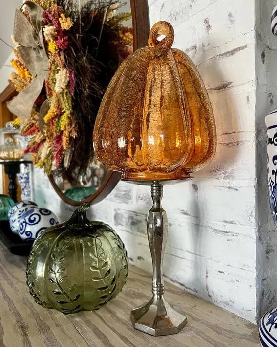 Close-up of glass pumpkins in amber and green tones on a fall mantel.