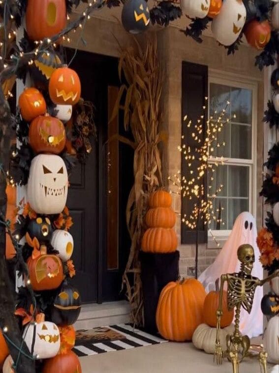 A stunning Halloween porch featuring a towering arch made entirely of intricately carved jack-o'-lanterns in shades of orange, white, and black, each with its own playful expression. 