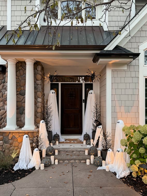 This porch makes a bold Halloween statement with a family of floating ghost figures, draped in flowing white fabric, creating a spooky yet charming vibe. 