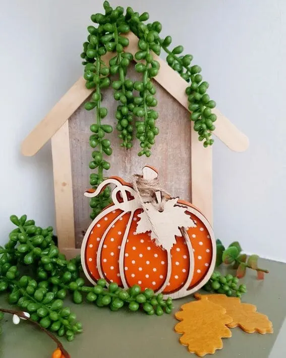 Polka dot pumpkin with cascading greenery and wooden leaves in a cozy fall display. 