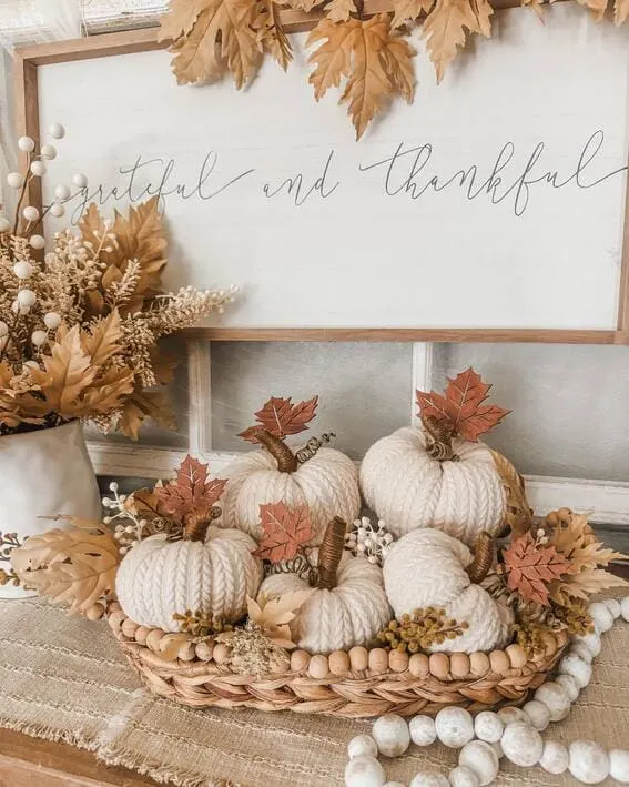 A soft and neutral fall display featuring knit pumpkins, wooden accents, and a warm autumnal palette—