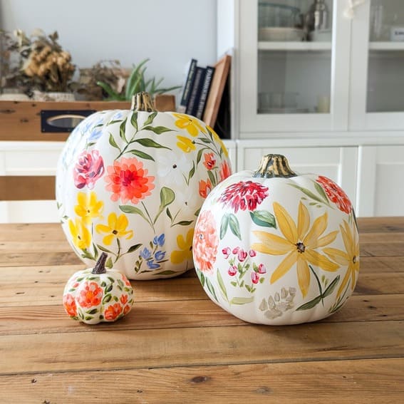 A beautiful trio of hand-painted pumpkins featuring vibrant floral designs in a mix of bright, cheerful colors. 