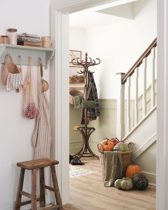 A charming entryway featuring a basket filled with pumpkins in natural tones, paired with warm wood accents and autumnal textures. 