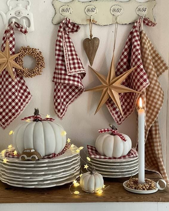 A cozy cottage-style display featuring white pumpkins, gingham linens, and star-shaped string lights for a rustic autumn vibe. 