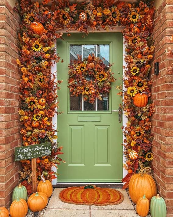 A festive door display features a lush autumnal garland of pumpkins, sunflowers, and fall leaves framed by a coordinating wreath.