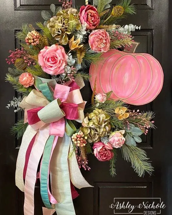 A vibrant, asymmetrical wreath featuring a hand-painted pink pumpkin, lush florals, and multicolored satin ribbons. 