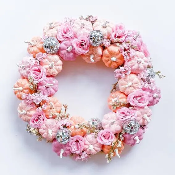 A vibrant wreath featuring pastel pink and orange pumpkins adorned with faux roses and disco balls for a whimsical, glamorous touch. 