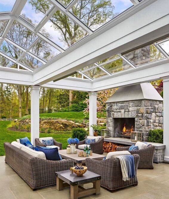 Beautiful patio with the fireplace of a stone under a glass pergola to give an airy yet cozy appearance. 