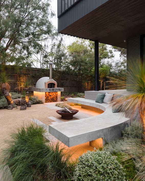 Modern outdoor space with the curved fire pit made of concrete and a built-in seating area with under-lighting. 