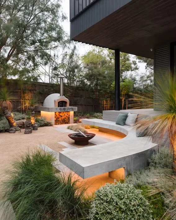 Modern outdoor space with the curved fire pit made of concrete and a built-in seating area with under-lighting. 