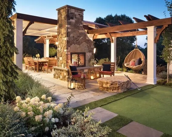 Outdoor dining space with an old-fashioned stone fireplace, comfy seating and pergola. 