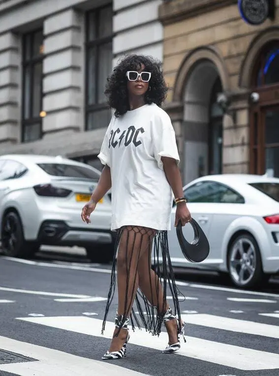 A woman in an oversized AC/DC graphic tee paired with fringe details and zebra-print heels. 