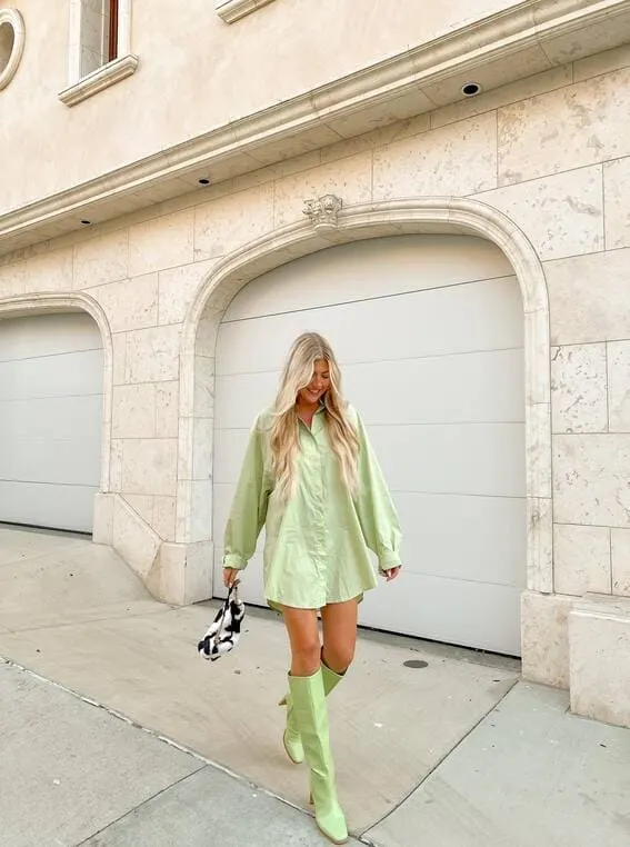 A stylish woman wearing an oversized light green shirt and matching knee-high boots. 