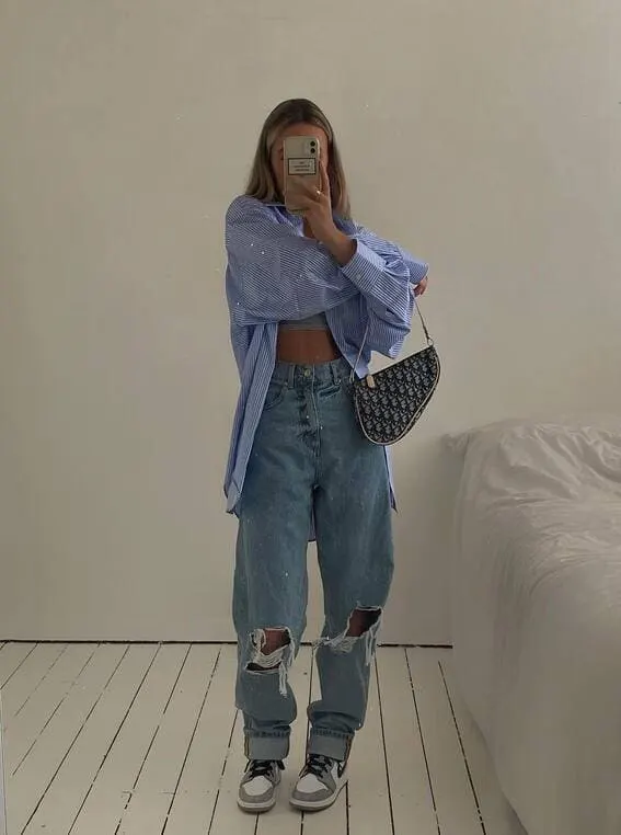 Trendy woman in a blue oversized shirt paired with distressed jeans and a designer bag. 