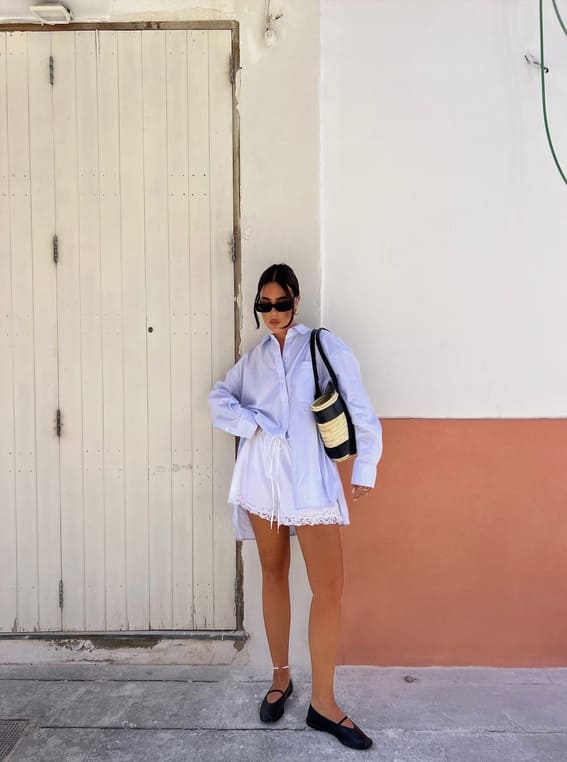 Chic woman wearing a white oversized shirt, lace-trimmed shorts, and a structured handbag. 