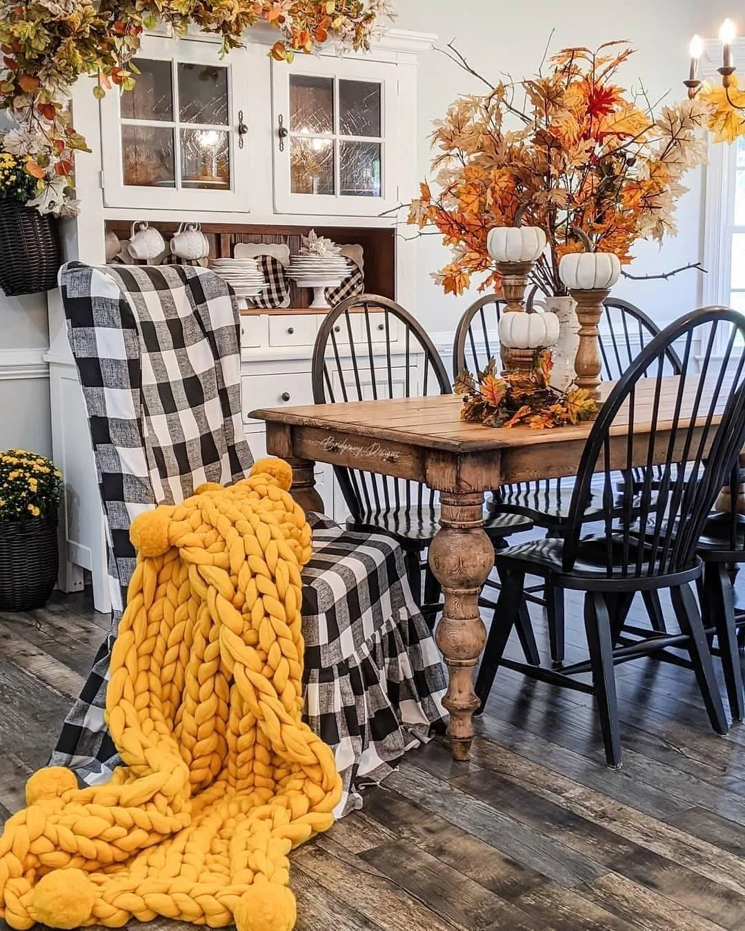 This image is a great idea for adding seasonal charm to a farmhouse dining room, featuring fall decor with cozy orange accents, a chunky knit blanket, and classic farmhouse furniture.Farmhouse dining room decor inspiration by @thosefarmhouseideas / Instagram